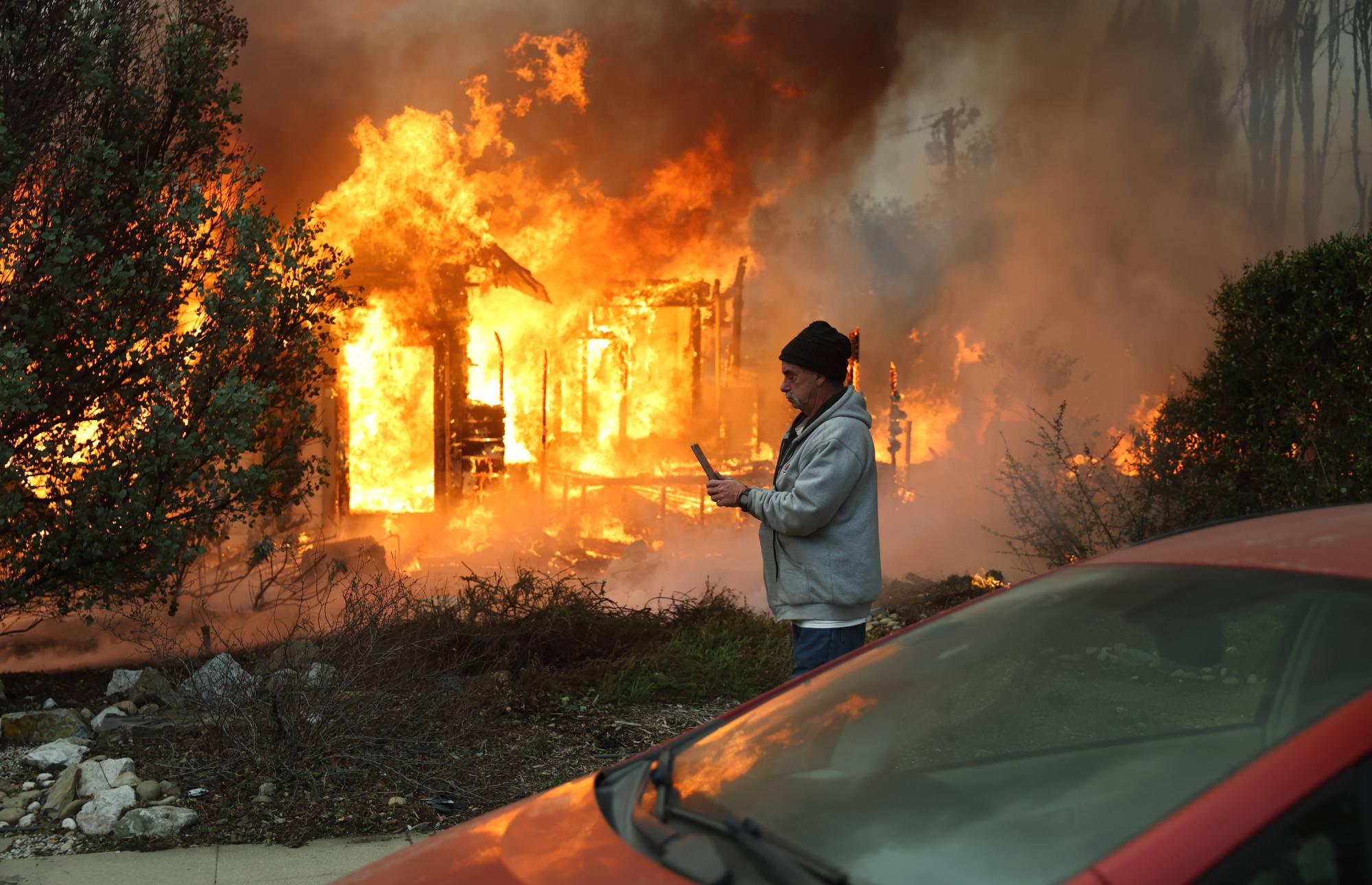 A person walks past a home burning during the Eaton Fire on Jan. 8 in Altadena. 